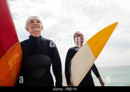 Coppia senior in wetsuit tenendo la tavola da surf in spiaggia Foto Stock