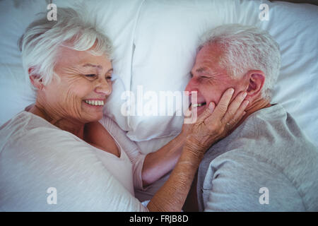 Senior donna holding marito guance mentre giaceva sul letto Foto Stock