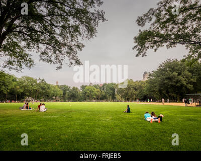 Gli spettatori della menzogna e della seduta su erba guardare la partita di baseball, al Central Park di New York City, Stati Uniti d'America. Foto Stock