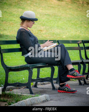 Donna seduta su banco del libro di lettura nel Central Park di New York City, Stati Uniti d'America. Foto Stock