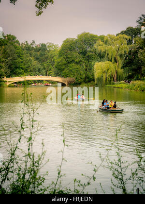 Barche a remi sul lago, Central Park, New York City, USA. Ponte di prua sullo sfondo Foto Stock