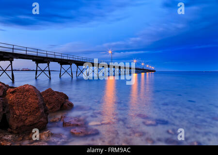 Basso punto di vista lungo pontile in legno e rocce costiere in Ceduna town bay quando acqua trasparente mostra fondali bassi di sunrise. Foto Stock