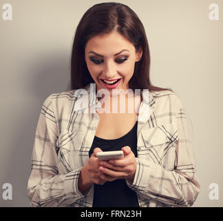 Felice sorprendente donna cercando in un telefono mobile e la lettura di sms con bocca aperta. Tonica closeup ritratto Foto Stock