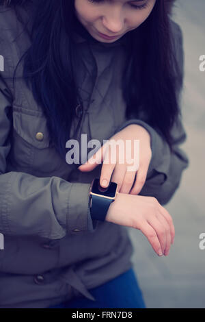 Bruna giovane ragazza in parka con il suo smart watch. L idea è quella di rimanere sempre connessi a internet, news e le reti sociali da ovunque ci si trovi Foto Stock