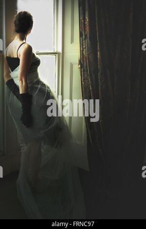Giovane ed elegante donna in piedi accanto alla finestra della vecchia casa Foto Stock