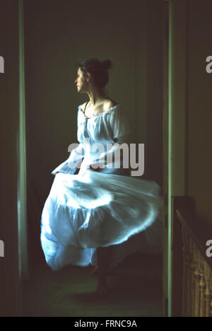 Giovane donna dancing in una vecchia casa indossando bianco lungo abito romantico Foto Stock