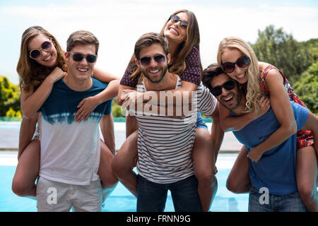 Tre uomini dando piggy bag a donne vicino alla piscina Foto Stock