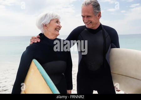 Coppia senior in wetsuit tenendo la tavola da surf in spiaggia Foto Stock