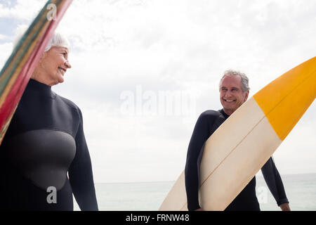 Coppia senior in wetsuit tenendo la tavola da surf in spiaggia Foto Stock