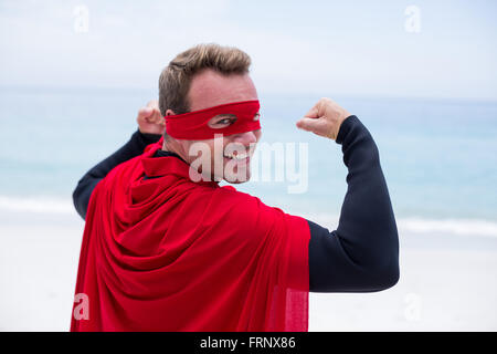 Uomo in costume da supereroe flettendo muscoli alla riva del mare Foto Stock