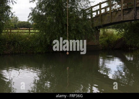 Una corda annodata appeso a un albero su un fiume, utilizzato come un altalena da bambini e ragazzi che giocano sulla riva del fiume nei pressi di un ponte nel Gloucestershire, UK. Foto Stock