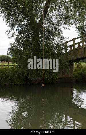 Una corda annodata appeso a un albero su un fiume, utilizzato come un altalena da bambini e ragazzi che giocano sulla riva del fiume nei pressi di un ponte nel Gloucestershire, UK. Foto Stock