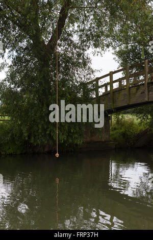 Una corda annodata appeso a un albero su un fiume, utilizzato come un altalena da bambini e ragazzi che giocano sulla riva del fiume nei pressi di un ponte nel Gloucestershire, UK. Foto Stock