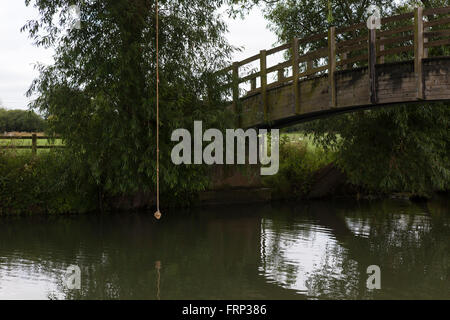 Una corda annodata appeso a un albero su un fiume, utilizzato come un altalena da bambini e ragazzi che giocano sulla riva del fiume nei pressi di un ponte nel Gloucestershire, UK. Foto Stock