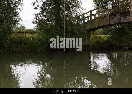 Una corda annodata appeso a un albero su un fiume, utilizzato come un altalena da bambini e ragazzi che giocano sulla riva del fiume nei pressi di un ponte nel Gloucestershire, UK. Foto Stock