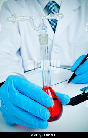 Primo piano di un giovane uomo caucasico in camice bianco con un pallone tarato con un liquido rosso in mano in un laboratorio Foto Stock