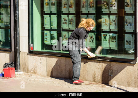 Kalmar, Svezia - 17 Marzo 2016: persona di sesso femminile la pulizia del Windows su un negozio. Essa utilizza un panno e ha il suo red secchio di acqua essere Foto Stock