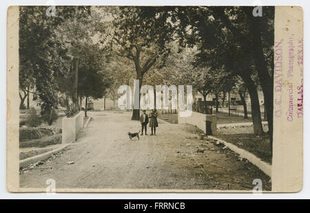 Una fotografia di bambini e un cane che giocano in un parco, con un ponte visibile sullo sfondo. La scena cattura un momento di svago e gioia, tipico della vita del parco dei primi anni del XX secolo, con soggetti umani e animali. Foto Stock
