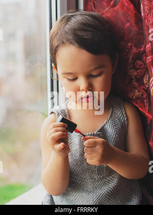 Piccolo bambino, carina ragazza toddler divertirsi giocando a casa con colorati per unghie facendo manicure Foto Stock