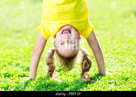 Ritratti di capretto felice giocando capovolto all'aperto in estate a piedi su mani sull'erba Foto Stock