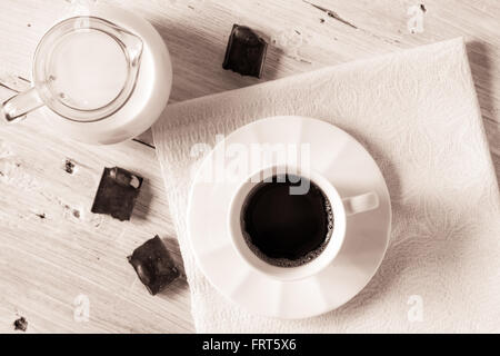 Tazza di caffè con la brocca del latte e cioccolato sulla tavola bianco vista superiore Foto Stock
