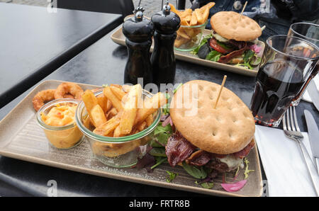 Due hamburger di manzo con pancetta, patatine fritte e anelli di cipolla servita su un paio di lunghe piastre quadrate Foto Stock