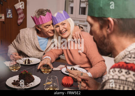 Felice coppia senior con corone di carta avente pudding natalizio Foto Stock