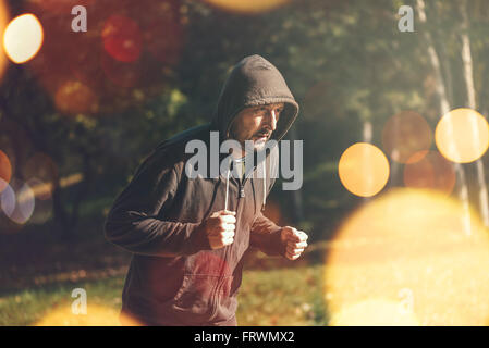 Uomo incappucciato jogging nel parco di inizio autunno mattina, uno stile di vita sano concetto, dai toni rétro immagine con il fuoco selettivo Foto Stock