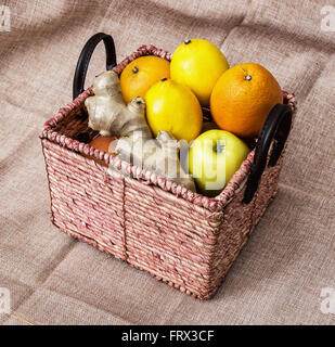 Cesto in Vimini con mele, arance, limoni e zenzero sul panno sfondo. Cibo sano. Foto Stock