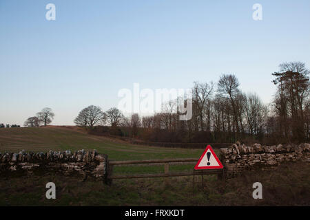 Un triangolo rosso cartello segnaletico si appoggia contro una parete del paese nei seguenti campi di Gloucestershire, UK. Con un punto esclamativo sul segno sembra essere la segnalazione di eventuali problemi nelle vicinanze. Foto Stock