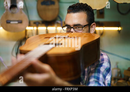 Liutaio shop e classici strumenti musicali: giovani adulti fissaggio artigianale vecchia chitarra classica. L'uomo guarda attentamente a ponte Foto Stock