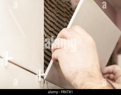 Lavoratore installatore mette le piastrelle di ceramica su una parete Foto Stock