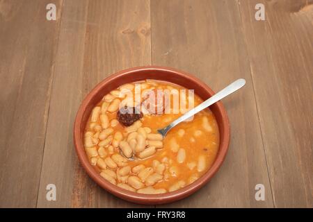 Asturiano stufato di fagioli in una pentola di creta su uno sfondo di legno vecchio Foto Stock