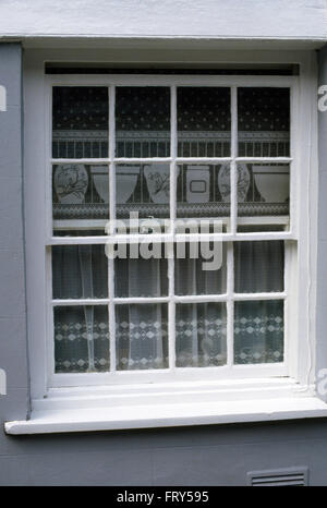 Close-up di un bianco finestra cottage con una decorazione a tendina di pizzo Foto Stock