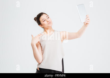 Giocoso attraente giovane donna business tenendo selfie con tablet e rendendo la faccia di anatra su sfondo bianco Foto Stock