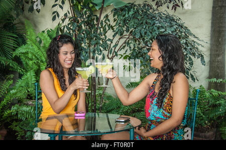 2 giovani donne ispaniche toast con margarita bevande sul patio tropicale - Puerto Vallarta, Messico #613PV Foto Stock