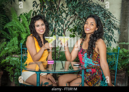 2 giovani donne ispaniche toast con margarita bevande nel patio tropicale - Puerto Vallarta, Messico #613PV Foto Stock