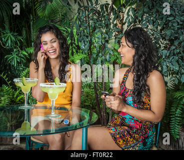 Ridendo giovani donne ispaniche con telefoni cellulari godetevi margarita bevande sul patio tropicale - Puerto Vallarta, Messico #613PV Foto Stock