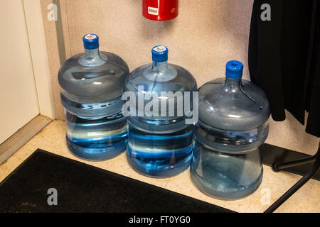 Tre 5 gallone di bottiglie di acqua sul pavimento di una zona di stoccaggio in un ufficio. Foto Stock