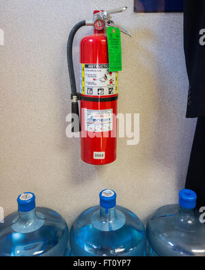Un obbligo di estintore appeso su una parete oltre 3 cinque galloni di acqua di bottiglie in un'area di memorizzazione di un'azienda. Oklahoma, Stati Uniti d'America. Foto Stock