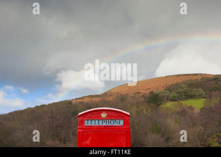 Un tradizionale britannico rosso nella casella Telefono siede sotto un grande arco arcobaleno su Bossington hill nel Somerset. Foto Stock