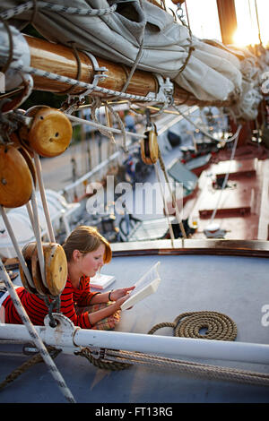 Adolescente sdraiato sul ponte della nave a vela durante la lettura di un libro, Lauterbach, Putbus, insland di Ruegen, Meclemburgo-Pomerania, Germania Foto Stock
