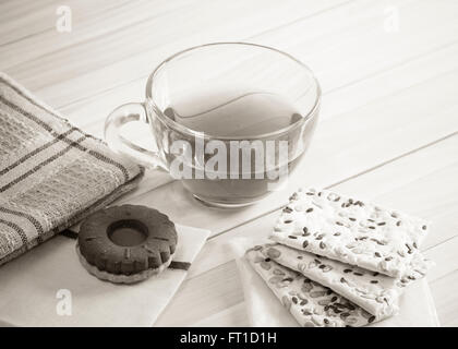 La composizione della bevanda di tè in una grande ciotola e alcuni dolci sul tavolo. I cookie di grano, bagel. Foto in bianco e nero. Foto Stock