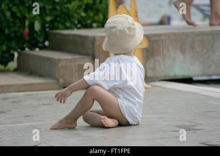 Ragazzo giovane lasciato solo molto vicino ad una piscina guardando la sua madre in uscita Foto Stock