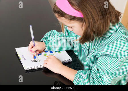 Bambina con un plaid verde smock il disegno di un dinosauro in un notebook a casa Foto Stock