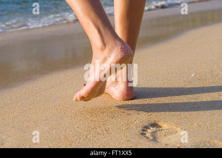 Spiaggia viaggio - donna camminando sulla spiaggia di sabbia lasciando tracce nella sabbia. Primo piano particolare del piede femminile e sabbia dorata Foto Stock