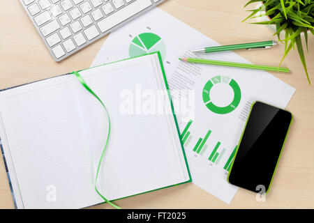 Scrivania in ufficio il luogo di lavoro con smart phone, grafici e blocco note su un tavolo di legno. Vista da sopra con lo spazio di copia Foto Stock