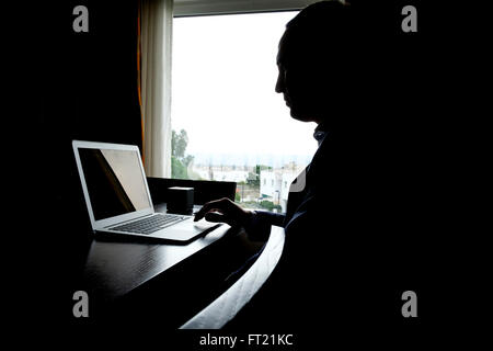 Silhouette di una persona che utilizza un computer portatile a casa Foto Stock