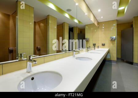 Toilette pubblica con una fila di gabinetti di fronte un grande specchio Foto Stock