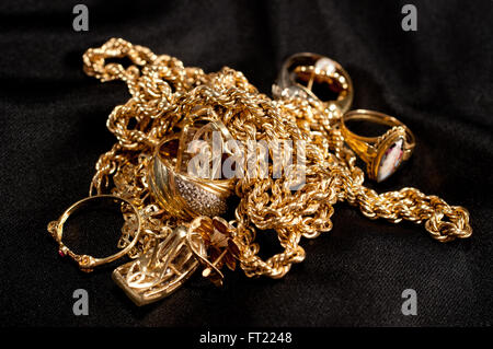 Rottami di gioielli in oro compresi catenelle, braccialetti e anelli su sfondo nero Foto Stock